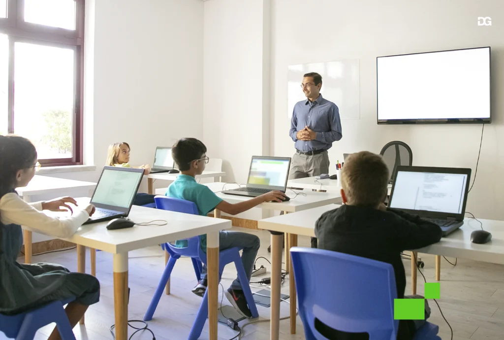 Professor ensinando alunos em sala de aula com computadores, integrando educação e tecnologia.